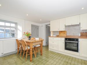 una cocina con armarios blancos y una mesa y sillas de madera. en Manor Cottage Barn, en Callington