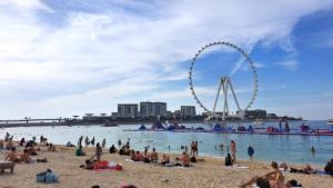 people on a beach with a ferris wheel in the background at The White Stay in Dubai