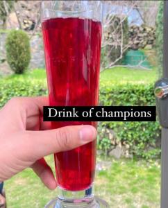 une main tenant un verre avec une boisson rouge de champions dans l'établissement Heritage Rose Inn, à Srinagar
