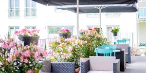 eine Terrasse mit Blumen, Stühlen und einem Sonnenschirm in der Unterkunft Hotel Das Augustin in Sankt Augustin