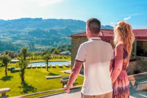 un homme et une femme debout sur un balcon donnant sur un jardin dans l'établissement Vale da Fonte - Charming Houses, à Ponte da Barca
