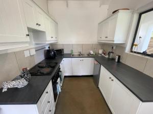 a kitchen with white cabinets and a black counter top at The Stables, Central Garden Cottage in Howick in Howick