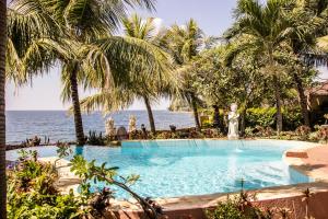 a swimming pool next to the ocean with palm trees at Teluk Indah Beach & Pool Villa in Tejakula