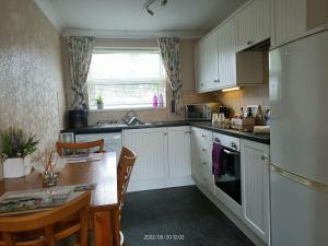 uma cozinha com armários brancos, uma mesa e um lavatório em Cromarty Cottage Eastbourne em Pevensey