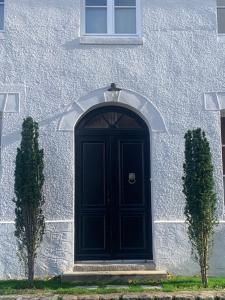 une porte noire sur un bâtiment blanc avec deux arbres dans l'établissement Chambre Suite d'hôte à Ouville la Rivière Normandie, à Ouville-la-Rivière