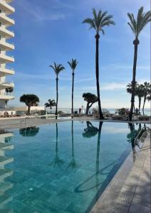 a pool with palm trees and the ocean in the background at Apartamento privado en Hotel Sol Aloha in Torremolinos