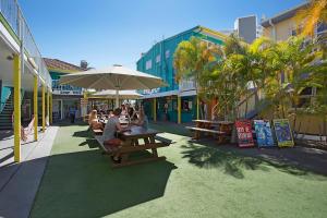a group of people sitting at tables under an umbrella at Backpackers In Paradise 18-35 Hostel in Gold Coast