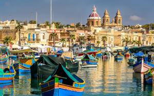 un groupe de bateaux amarrés dans un port avec des bâtiments dans l'établissement BaySide1 Marsaxlokk Malta, à Marsaxlokk