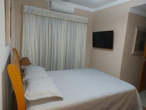 a small bedroom with a bed and a television at Flat Pitangueira com Piscina-Capitânia Varan in Guarujá