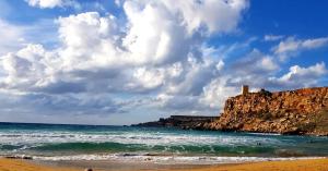 a view of a beach with a lighthouse on a cliff at Village Getaway - Mgarr Malta in Mġarr