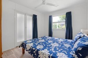 a bedroom with a bed with a blue comforter and a window at The Shack Rainbow Beach - Pets Welcome - Fully Fenced - Close to Beach in Rainbow Beach