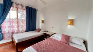 a room with two beds and a window with blue curtains at Hostal Nuevo Arenal downtown, private rooms with bathroom in Nuevo Arenal