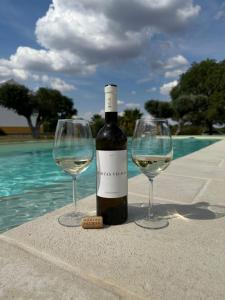 a bottle of wine and two wine glasses next to a pool at Monte das Hortas Velhas in Viana do Alentejo