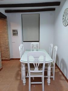 une table avec des chaises blanches et une horloge sur le mur dans l'établissement La casita Ronda, à Ronda