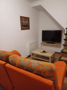 sala de estar con sofá naranja y TV de pantalla plana en La casita Ronda en Ronda