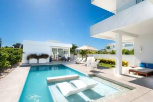 a swimming pool with chairs and a house at Beachside 3 Bedroom Villa with Pool and Resort Amenities - White Villas - v4 in Providenciales