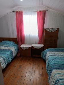 a bedroom with two beds and a window and wooden floors at Cómoda Casa en sector residencial Osorno in Osorno