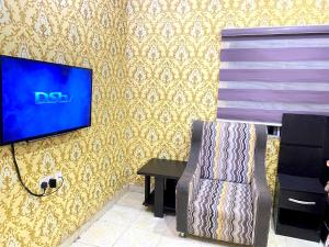 a tv on a wall with a chair and a table at DIVINE VILLA AND RESORTS HOTEL GUEST House 15 mins Near Michael Okpara University Sam Mbakwe Airport in Umuhu +16 photos