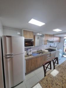 a kitchen with a white refrigerator and wooden cabinets at Apto luxo de 2 quartos, 3 banheiros Praia do forte in Cabo Frio