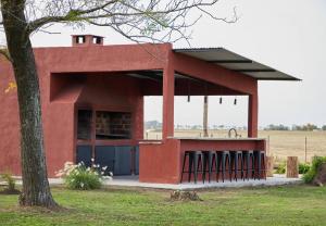 ein rotes Gebäude mit einem Baum auf einem Feld in der Unterkunft Hestia At San Antonio De Areco I Estancia Paraso in San Antonio de Areco