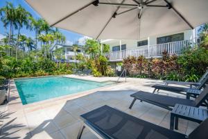 a swimming pool with an umbrella and two chairs at Unit 15 @ Tropical Reef: 2 mins to Four Mile Beach in Port Douglas
