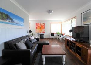 a living room with a black leather couch and a flat screen tv at Breakaway, 11 Scott Street in Crescent Head