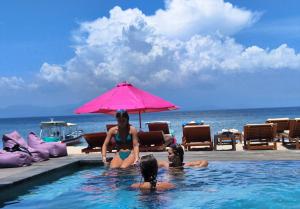 zwei Frauen sitzen in einem Swimmingpool mit Sonnenschirm in der Unterkunft Lushy Hostel Nusa Penida in Nusa Penida