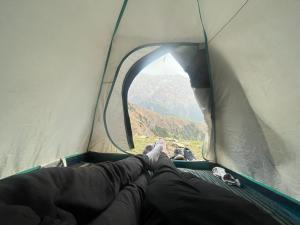 a person laying in a tent looking out the window at Triund Trek in Dharamshala