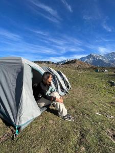 a man sitting inside of a tent in a field at Triund Trek in Dharamshala