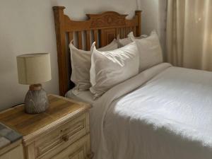 Cama con almohadas blancas y mesa con lámpara en Jane's Guesthouse, en Saldanha