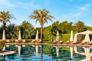 einen Pool mit Stühlen, Sonnenschirmen und Palmen in der Unterkunft Kempinski Hotel The Dome Belek in Belek