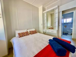 a bedroom with a white bed with red and blue pillows at The Perfect Hartenbos Holiday Home in Mossel Bay
