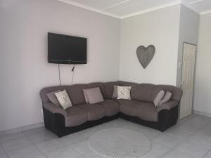 a living room with a brown couch and a flat screen tv at Oppi Draai Guesthouse in Oudtshoorn