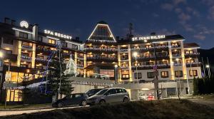 a large building with two cars parked in front of it at Family Luxury Private Apartment for 4 max 6 people in 4 star SPA Resort St Ivan Rilski, Bansko in Bansko