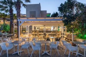 un restaurante al aire libre con mesas, sillas y palmeras en Gouves Bay by Omilos Hotels, en Gouves