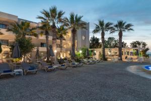 a hotel with chairs and palm trees in front of it at Gouves Bay by Omilos Hotels in Gouves
