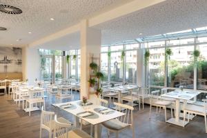 un restaurante con mesas y sillas blancas y ventanas en NH Hamburg Mitte, en Hamburgo