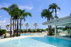 a swimming pool with palm trees and a building at Mia Resort Paestum in Paestum