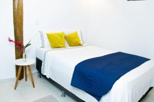 a white bed with a blue blanket and yellow pillows at Suítes Margarida in Ubatuba