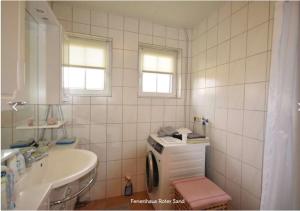 a white tiled bathroom with a sink and a toilet at Haus Roter Sand in Hooksiel in Wangerland