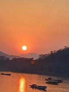 una puesta de sol en un río con barcos en el agua en Mekong Backpackers, en Pakbeng