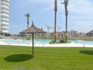 ein Resort mit einem Pool und einem Sonnenschirm im Gras in der Unterkunft Global Properties, Moderno apartamento de dos terrazas con increibles vistas al mar in Canet d'en Berenguer