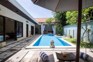 an outdoor swimming pool with an umbrella next to a house at Enigma Bali Villas Complex Canggu in Canggu