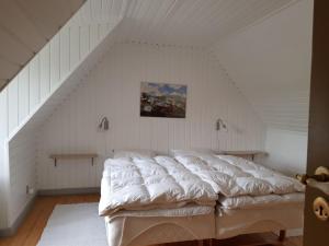 a bedroom with a white bed in a attic at Pyttegården Apartments in Gudhjem