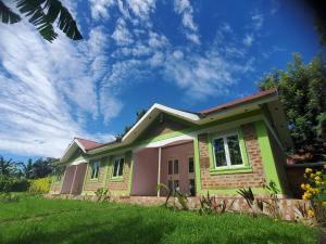 a green and pink house with a blue sky at Havannah Campsite and Homestay in Fort Portal