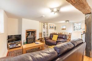 a living room with a leather couch and a television at 1 Ruscon Cottage in Brancaster