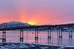 un puente sobre un cuerpo de agua con una puesta de sol en Leilighet ved porten til Senja. en Finnsnes