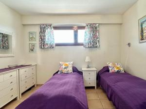 - 2 lits dans une chambre avec des draps violets et une fenêtre dans l'établissement Bonito Apartamento Con Piscina y Jacuzzi, à L'Alfàs del Pi