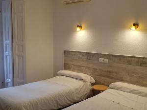 um quarto com duas camas e duas luzes na parede em Hostal Ginebra em Madri