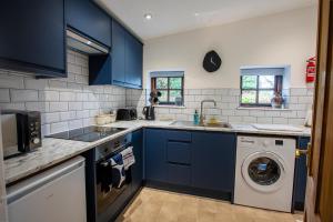een keuken met blauwe kasten en een wasmachine en droger bij The Carriage House a relaxing 1-Bed Cottage in Ash in Ash